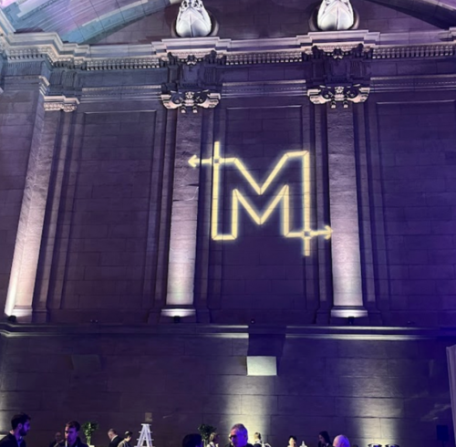 Conference participants talk to each other under a large letter M